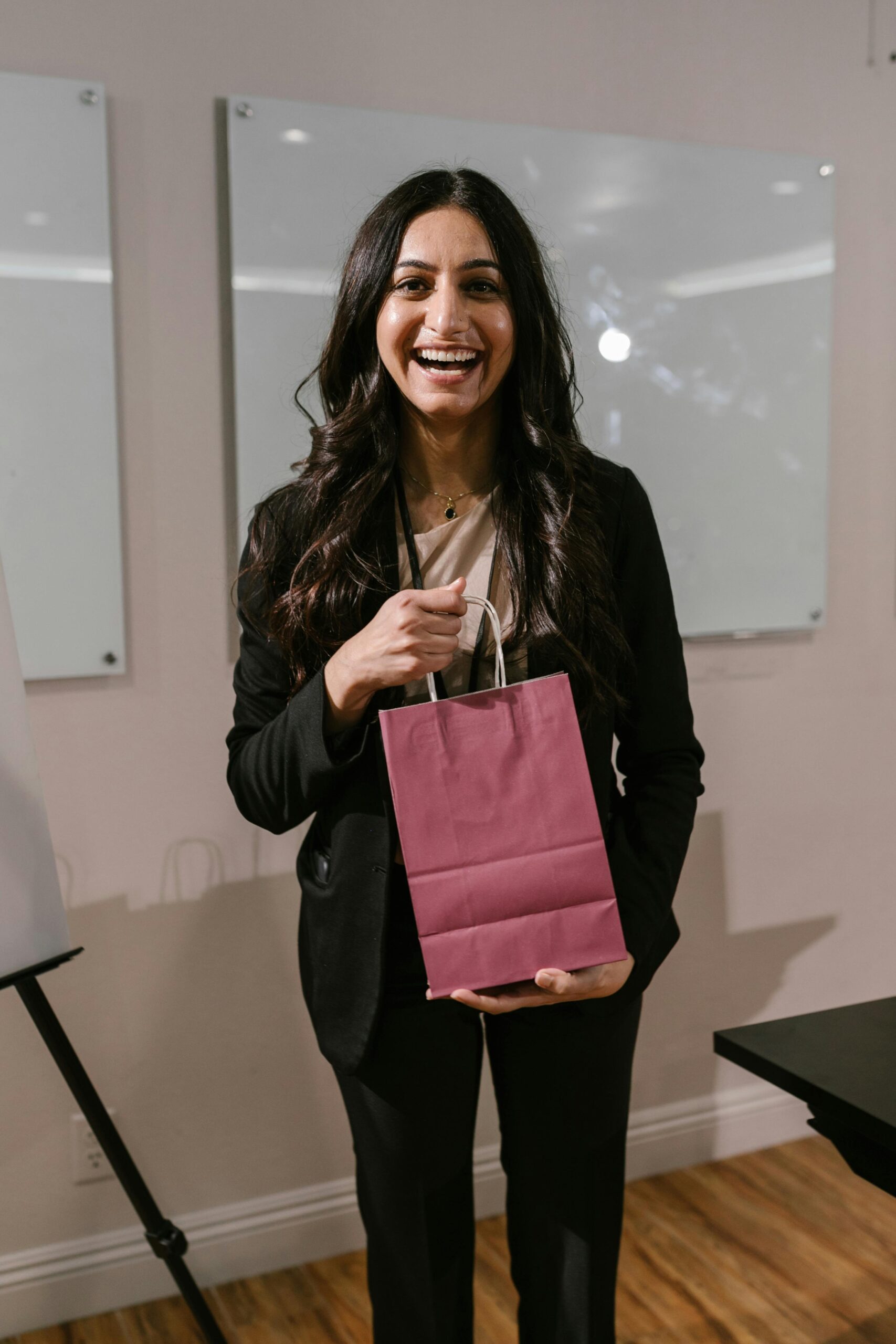 Confident woman in office holding a gift bag, showcasing a positive and professional atmosphere.