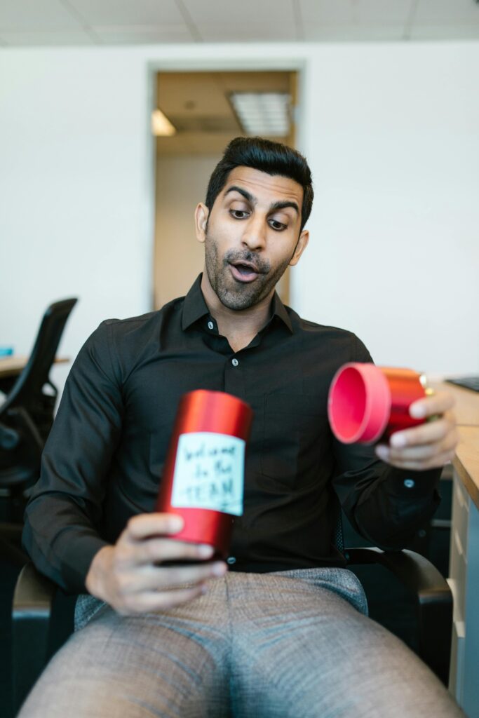 Man in office with a surprised expression holding an open gift. Workplace celebration.