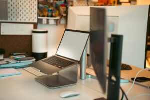 Contemporary home office space featuring a blank laptop screen on a stand, surrounded by notebooks and monitors.