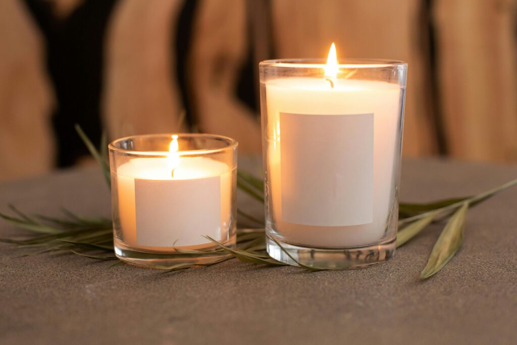 Minimalist candles in glass containers with blank labels, surrounded by leaves.
