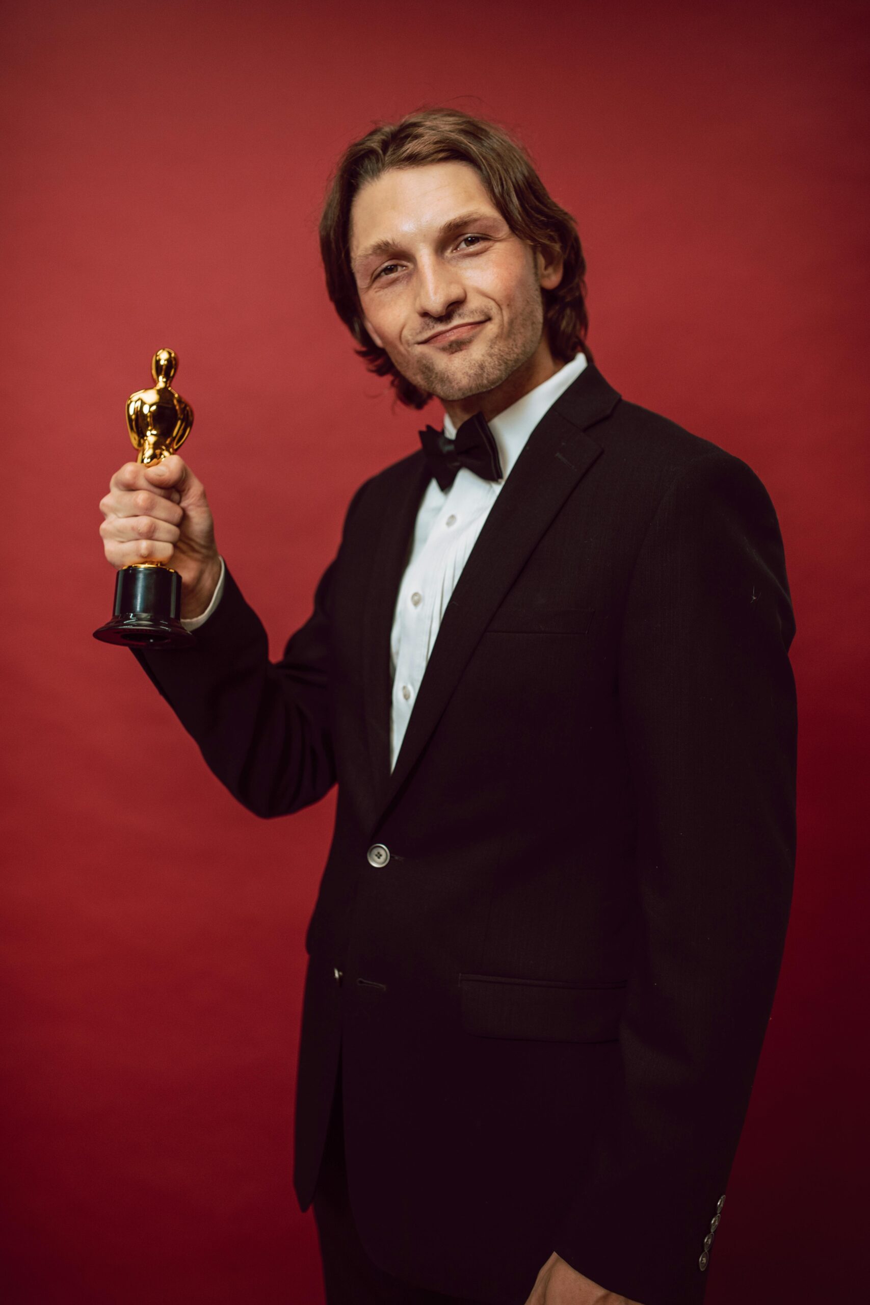 A man in formal attire proudly holds a trophy against a red background, symbolizing success and recognition.