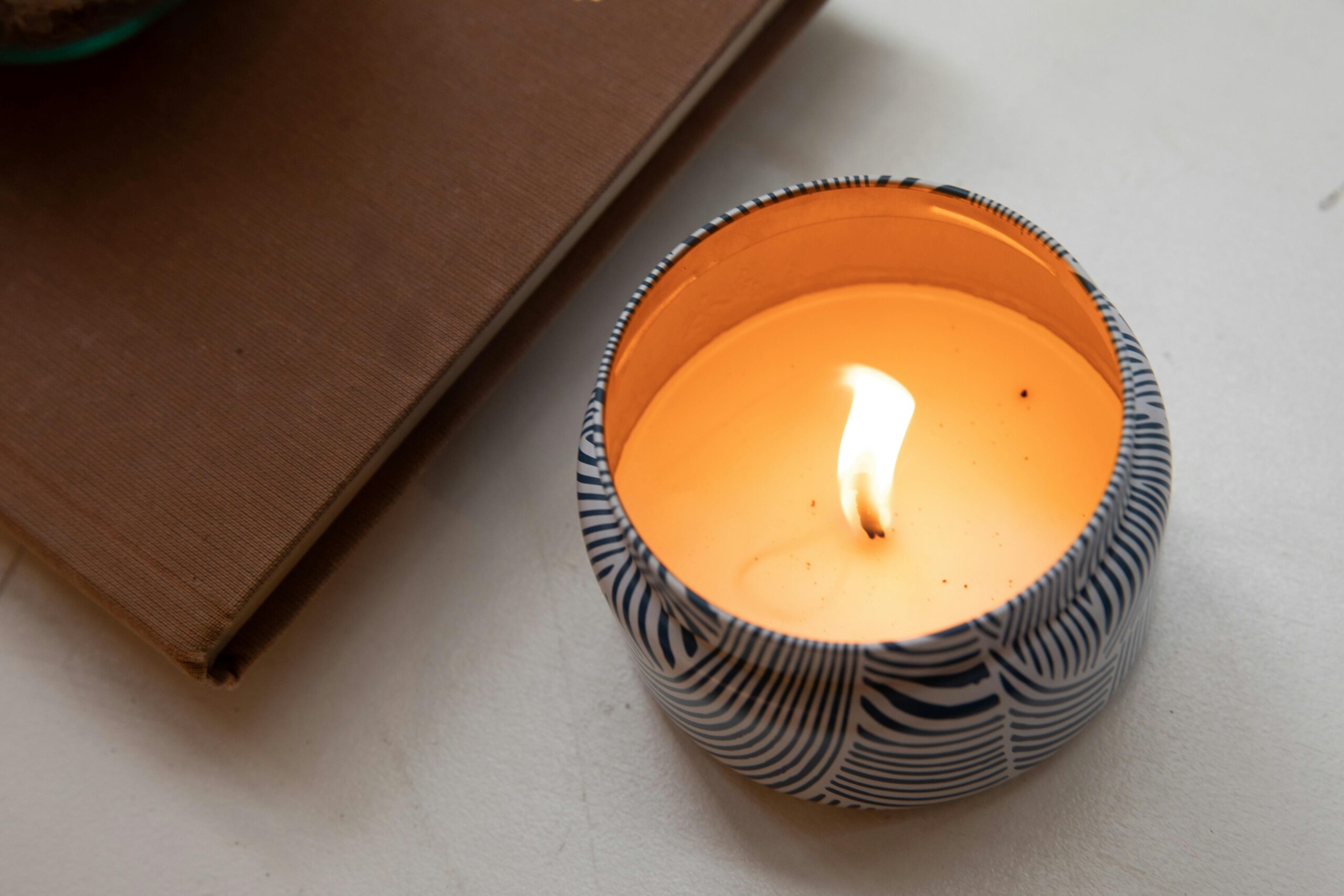 A close-up of a lit candle in a patterned holder on a table next to a book.